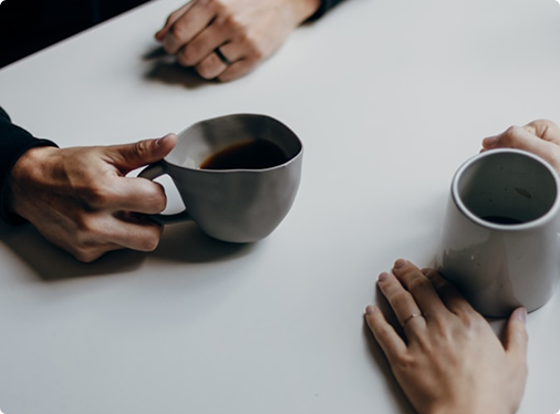 Zwei Menschen mit Kaffeetassen in einem persönlichen Gespräch.